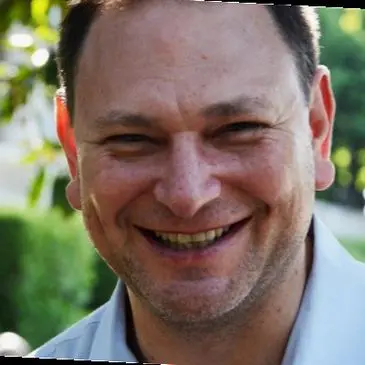 A man smiling for the camera in front of trees.