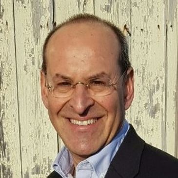 A man with glasses and a suit smiling.