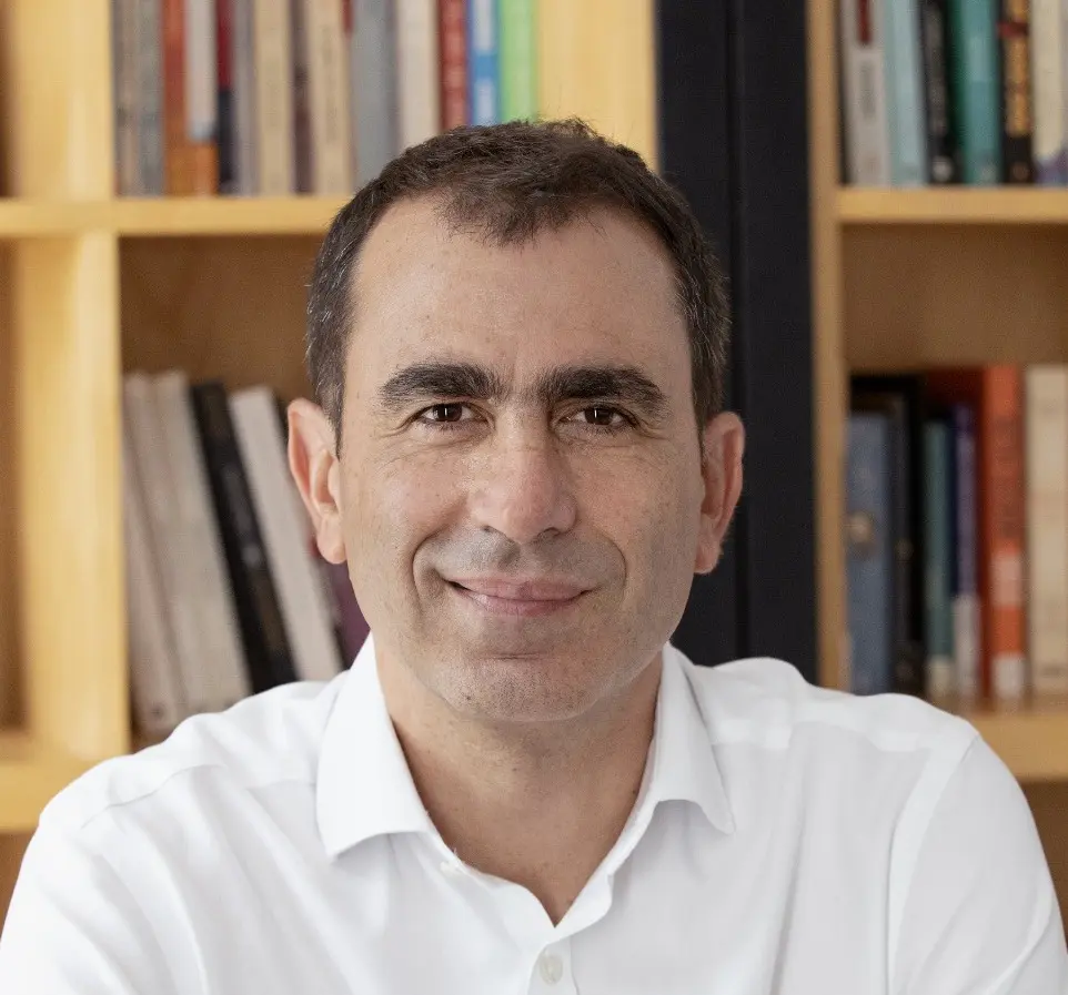 A man in white shirt sitting next to book shelf.